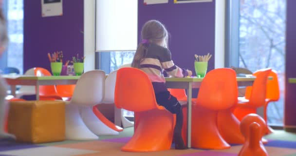 Het meisje zit in eenzaamheid op een oranje stoel in de buurt van de plastic tafel. — Stockvideo