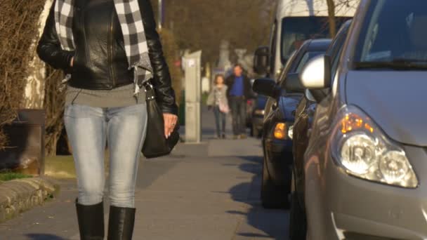 Kvinnan promenader av trottoaren närheten av parkerade bilar stadens torg i Opole Polen staden dag människor gå av en gata längs vägen solig dag våren — Stockvideo