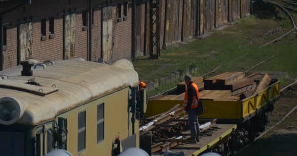 Pracovníci v oranžových pracovních oděvech Pracovníci na žluté plošině lokomotivy s železničními pražci Železniční uzel nádraží Polsko Opolský slunečný den — Stock video