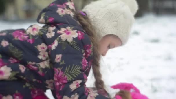 Yığın, kar kış küçük kız gülümseyerek binalar kar buz gibi kız çiçekli ceket ve pembe pantolon kadar yükselterek bir yer kapmak için çocuk oturur — Stok video