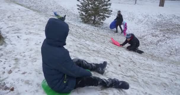 Kids Ride on the Plastic Sledges From Hill in the Park Ground Coberto com neve Dia de Inverno nevado Kiev Ucrânia — Vídeo de Stock