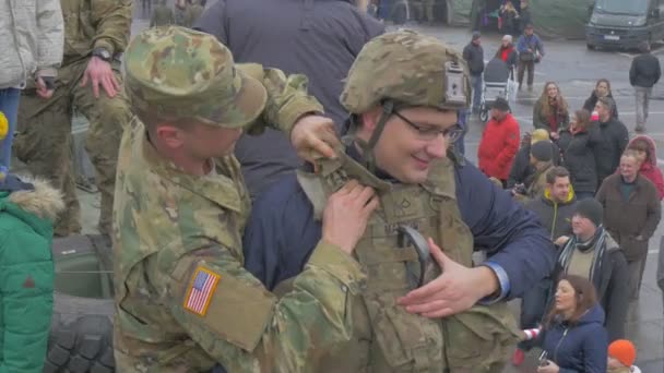 兵士はオポールの人々がイベント兵士が公共を楽しませるのを見て、都市広場で歩いているオポールの迷彩NATO作戦で市民の男をドレッシングしています — ストック動画