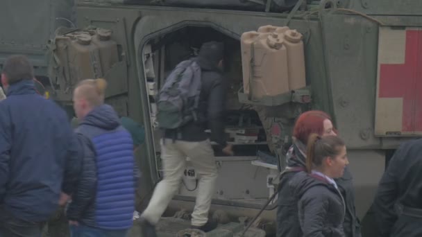 Люди проходят мимо открытого кабинета грузовика НАТО операции в Опольских солдатах и военных транспортных средствах Люди смотрят парад в День облаков на городской площади — стоковое видео