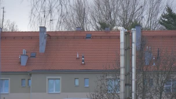 Gebäude bei Sonnenuntergang Strahlen blanker Rauch von Rohrheizung Schornstein rot Dach kahle Äste Bäume Fenster früh Frühling oder spät Winter tagsüber Abend sonniger Tag — Stockvideo