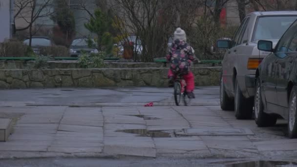 Kid je jízda na kole a ztratí její rukavice Park chodníku dlažební dlaždice zaparkované auta holé větve stromů holčička v květovaný kabátek večerní panoráma — Stock video