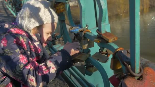 Kid is Looking at the Padlocks Terkunci di Bridge Metal Rods Symbol of Eternal Love Marriage Wedding Tradition Bridge Over River Sun Reflection in a Water — Stok Video