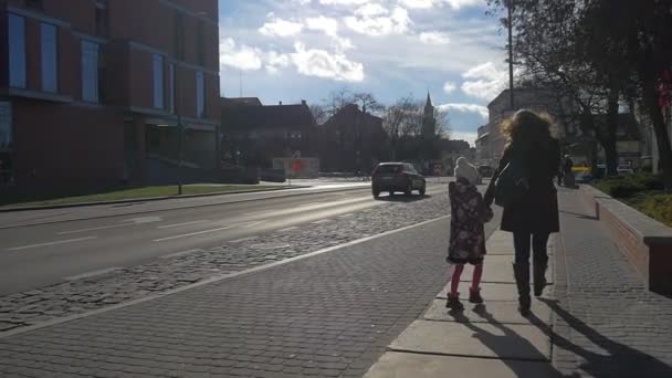 Mum and Daughter Walk by Cobblestone Street Cityscape Opole Pedestrians in Warm Clothes on a Sidewalk Cars Are Driven Bare Branches Trees Sunny Day Winter — Stock Video