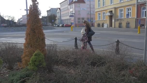 Vrouw en kind krijgen rond een droog gazon weg lopen door de straat Cityscape Opole voetgangers in op een trottoir oude gebouwen groenblijvende decoratieve bomen — Stockvideo