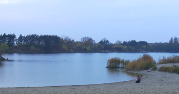 Homme avec ordinateur portable à la rivière Lake Sandy Bank Homme d'affaires Freelancer Arbres à la rive opposée dans un crépuscule vert et jaune Herbe Smooth Water Automne — Video