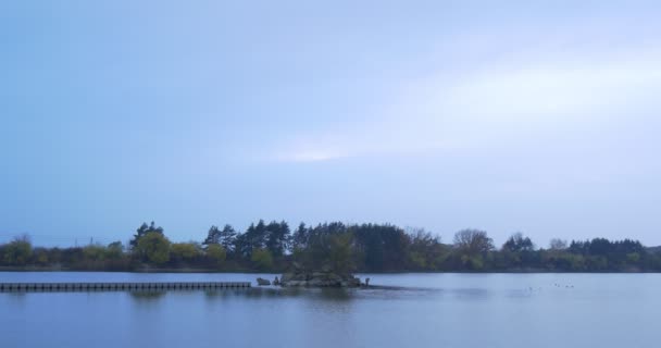 Holzsteg in der Mitte eines Flusses kleine Insel mit Bäumen bewachsen Herbstlandschaft gelbe und grüne Blätter Bäume auf der gegenüberliegenden Seite Flussufer Dämmerung — Stockvideo