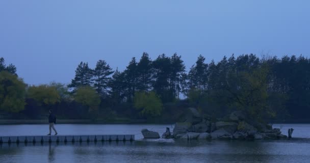 Stand turistici sul molo di cemento Passeggiate Lentamente piccola isola ricoperta di alberi Paesaggio autunnale Foglie gialle e verdi Alberi crepuscolari sul lato opposto — Video Stock