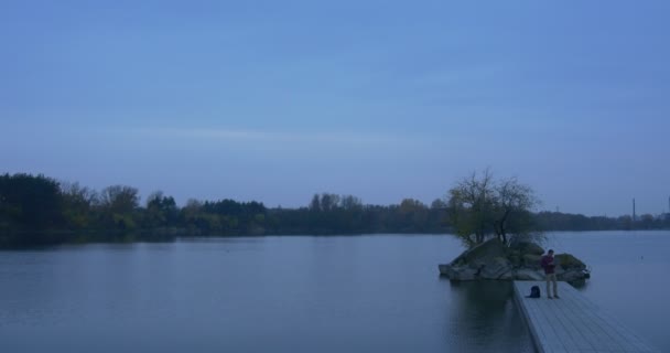 Mann arbeitet am Laptop auf einem Steg Spaziergänge nimmt eine Tasche kleine Insel auf einem Fluss mit Bäumen bewachsen Herbst Landschaft Abenddämmerung Geschäftsmann Freiberufler im Freien — Stockvideo