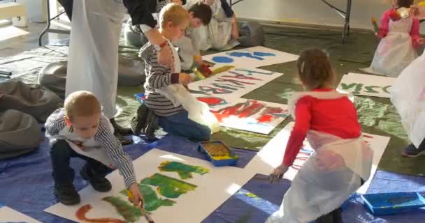 Семейный мастер-класс "Опольские дети" рисуют буквы на полу, раскрашивая бумагу, которую люди рисуют в детском саду — стоковое видео
