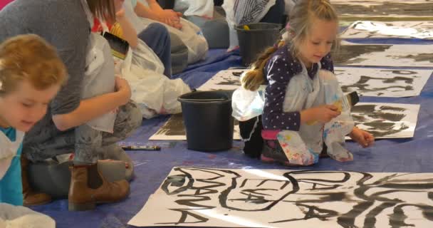 Familia Master Class Galería de Arte Opole Kids Escribir palabras en una pintura de papel Educadores negros ayudan a los niños La niña está pintando en el suelo se levanta — Vídeos de Stock