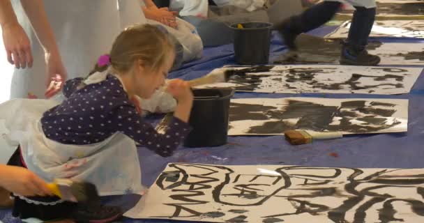 Familjen Master Class Art Gallery Opole pojkar flickor skriva ord på ett papper målning svart pedagoger hjälpa är barn lilla flickan målning sitter på ett golv — Stockvideo