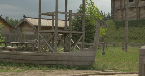 Holzboot auf der grünen Wiese, Mauer auf dem Hügel, Häuser, grauer Himmel — Stockvideo