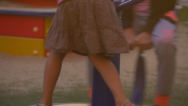 Children Are at The Playground at The Yard, Playing, Swinging,Children Legs Closeup, Girls on a Carousel, Girls in Pink and Black Blouses, Blonde — Stock Video