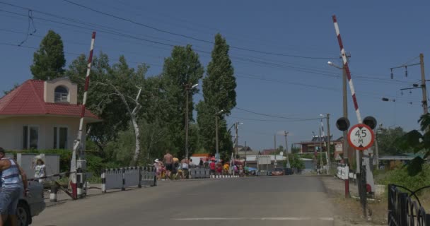 Asphalted Road Railroad Crossing, People Go by Road, Railway Workers House with Red Roof, Horizon, Blue Sky — Stock Video