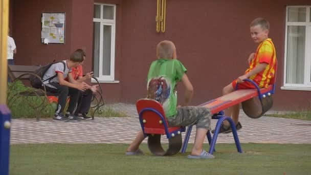 Los niños están en el patio de recreo en el patio, jugando, balanceándose, muchachos en un Teeter-Totter, adolescentes, muchachos en un banco — Vídeos de Stock