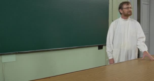 Professor, man, scheikundige, bioloog in White Medical robe houdt de klas, lezing aan het Bureau van de leraar, wandelen naar de deur, gang — Stockvideo