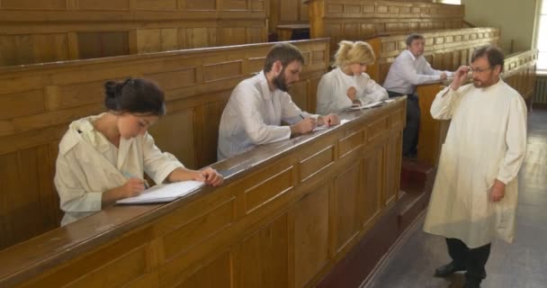 Profesor, químico, biólogo, profesor está llevando a cabo la lección, clase, delante de los estudiantes, caminando por el auditorio, los estudiantes están escribiendo — Vídeos de Stock