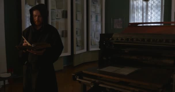 Μουσείο της εκτύπωσης, μοναχός είναι το περπάτημα με το βιβλίο του από την αίθουσα, αρχαία εργαλεία εκτύπωσης, άνθρωπος ανάγνωση, ξεφυλλίζει το βιβλίο — Αρχείο Βίντεο
