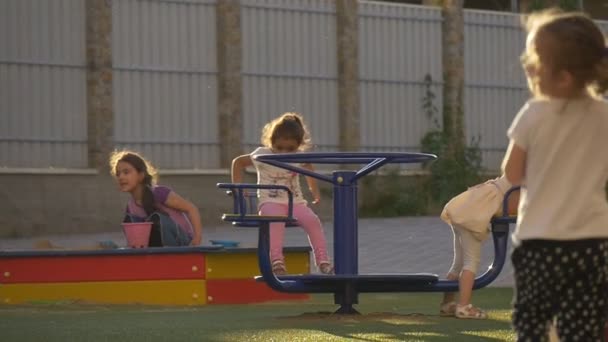 Crianças, crianças estão brincando em um parque infantil, balançando no carrossel, raios de sol, câmera lenta — Vídeo de Stock