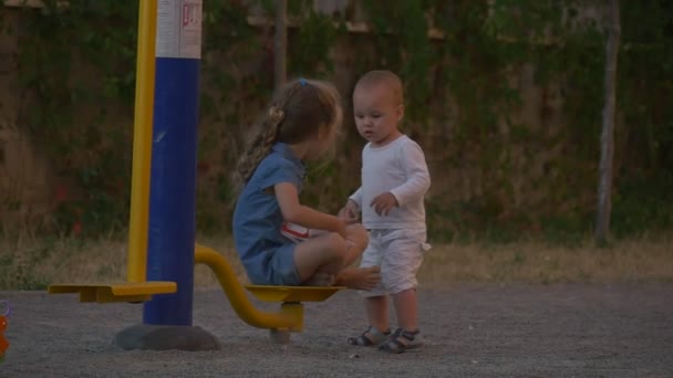 Menina em azul e menino em branco juntos no parque infantil — Vídeo de Stock