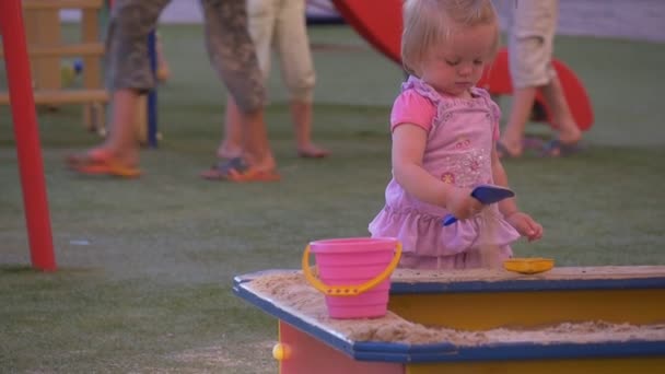 Μωρό, μικρό κορίτσι στο ροζ είναι παίζοντας σε ένα Sandbox, κοιτάζοντας τα παιδιά σε ένα αλεξίπτωτο, καλοκαιρινή μέρα — Αρχείο Βίντεο