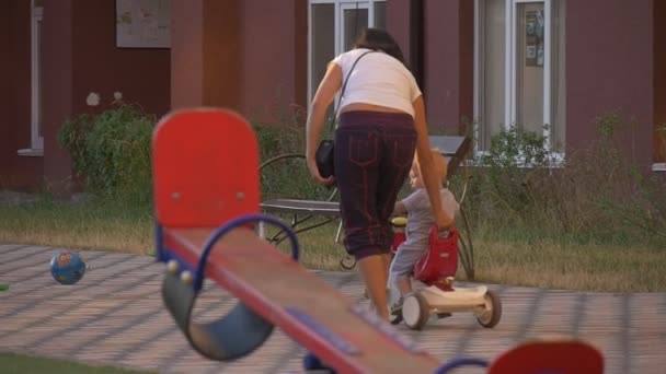 Kleine jongen met driewieler gaat over de werf verder — Stockvideo