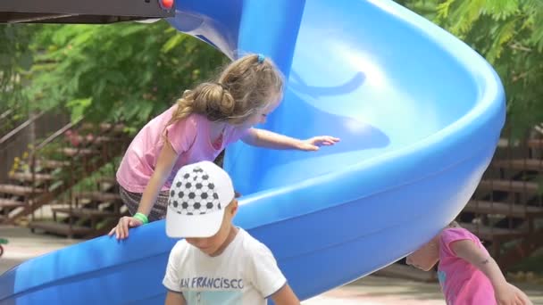 Bambini, Bambini che giocano al parco giochi, Ragazze che giocano sul paracadute blu, Arrampicata al paracadute blu, Ragazze in t-shirt rosa, Capelli biondi — Video Stock