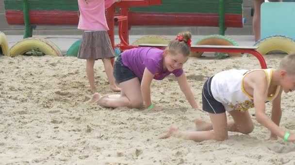 Los niños están jugando, el niño y la niña se arrastran por la arena, corriendo en el parque infantil Sandy — Vídeos de Stock