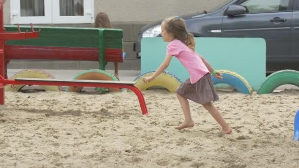 Enfants, Enfants jouent sur le terrain de jeu, Filles en T-shirts roses, avec des cheveux blonds, Fille court à travers le terrain de jeu, Sable, Suivi à gauche — Video