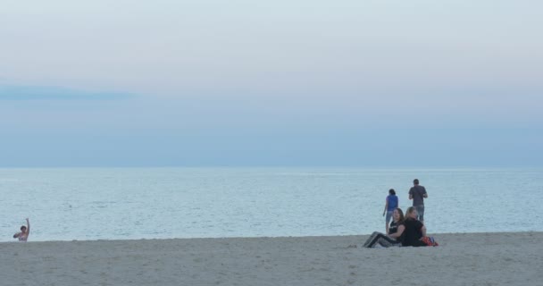 Люди, дітей, сімей, в піщаний пляж, відпочиваючи, ранній вечір, пара наближається до моря, жінки повернулися сидить на задній план — стокове відео