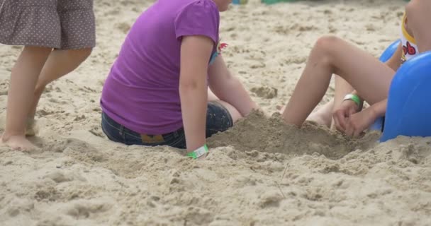 Kinder spielen, auf dem sandigen Spielplatz sitzen Jungen und Mädchen in violettem T-Shirt an der blauen Rutsche, sandiger Boden, gegrabene, lackierte Reifen — Stockvideo