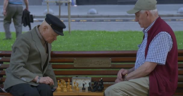 Deux hommes sont assis l'un devant l'autre sur le banc, Hommes âgés âgés dans des casquettes, Jouer aux échecs, Mid Shot, Prendre les virages rapidement — Video