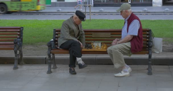 Dwóch mężczyzn są siedząc sobie na ławce, Senior w wieku mężczyzn w czapki, gra w szachy, połowie strzał — Wideo stockowe