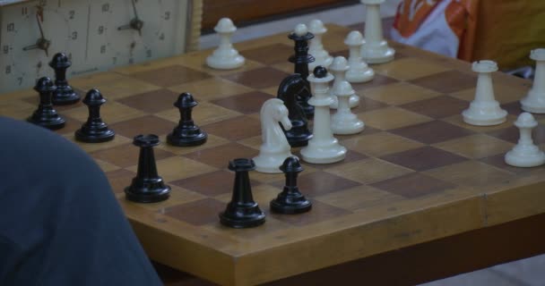 Due uomini sono seduti uno di fronte all'altro sulla panchina, giocando a scacchi, accendere gli orologi a scacchi, primo piano della scacchiera, scacchi dipinti in bianco e nero — Video Stock