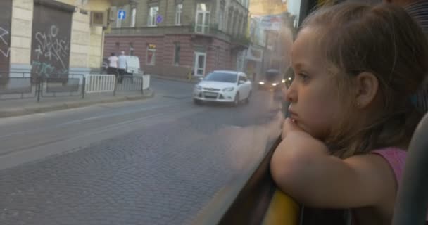 Niña rubia está sentada en la ventana del autobús, mirando a través de la ventana del Lviv, la gente, los pasajeros, los coches, la chica se han inclinado la cabeza — Vídeo de stock