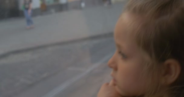 Petite fille blonde est assise à la fenêtre dans le bus, regardant par la fenêtre à la Lviv, les gens passent, voitures, fille ont penché la tête — Video