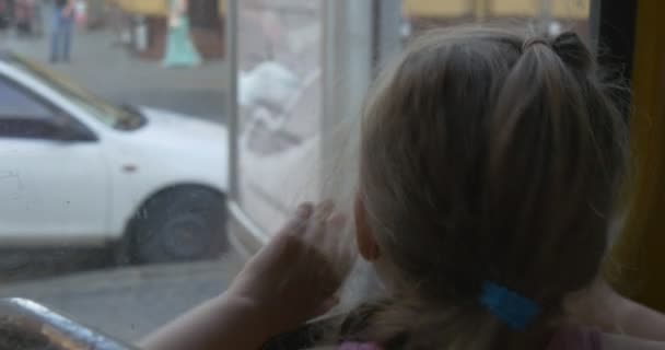 Kleines blondes Mädchen in rosa Hemd sitzt am Fenster in Bus, Straßenbahn, Obus, schaut durch das Fenster auf lviv, Mädchen lächelt, redet — Stockvideo