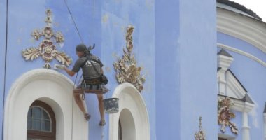 Restoratör, erkekte siyah T-Shirt, endüstriyel tırmanıcı, duvar, duvar dekore edilmiş altın elemanları ile bileme duvar boyama bir ip üzerinde tutuyor