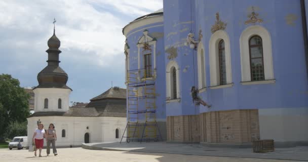 Murs bleus de St. Michael's Cathedral, Réparation, Restaurateurs, Hommes, Escalades industrielles, Les gens passent, Église blanche sur fond — Video