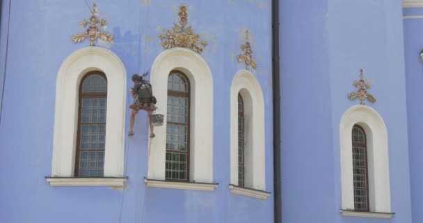 Restaurátor tart egy kötelet, ipari mászó között két Windows a székesegyház, festékek, egy vödör, a férfi festészet a St. Michael székesegyház — Stock videók