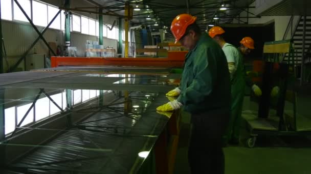 Três trabalhadores estão tirando as peças de vidro após o corte por robô, os trabalhadores estão em capacetes de segurança laranja, produção de vidro — Vídeo de Stock