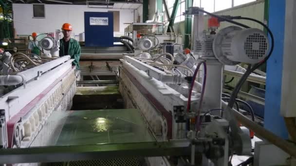 Dos trabajadores en cascos de seguridad naranja, hoja de vidrio está en Mashine, máquina para biselado, fabricación de chaflán, molienda de borde de vidrio — Vídeos de Stock