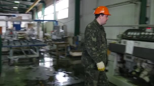 Werknemer in oranje helm benadert de machine, drukt op de knop, de machine draaien, een andere werknemer staat op de stand met plaatglas — Stockvideo