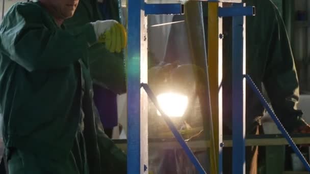 Trzech robotników w fabryce Uniform, pracownik w Orange kask bezpieczeństwa, rękawice, są niosące arkusz szkła, ustanowienie arkusza w metalowej ramie — Wideo stockowe