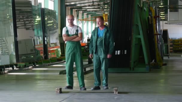 Doi muncitori în uniformă verde, stau la foaia de sticlă, foaia se află orizontal pe două blocuri, se oprește pe foaie, omul în civil — Videoclip de stoc