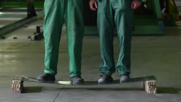 Dois trabalhadores em uniforme verde, botas, colocar a folha de vidro em dois blocos, homens parados até o vidro, balançado, testado o vidro, vidro não quebrou — Vídeo de Stock